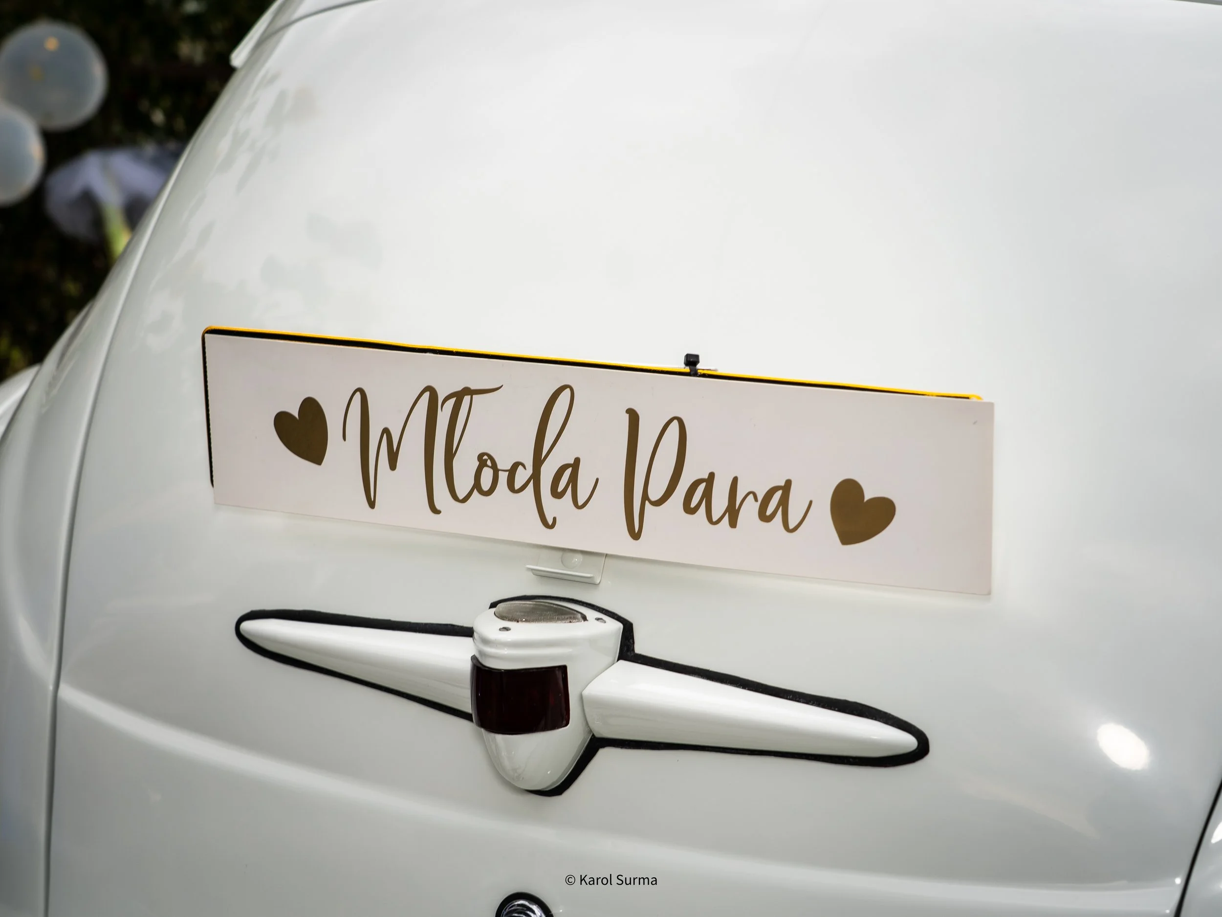 Vintage white car with a sign that says 'MtoDa Para' decorated with two brown hearts, and a small airplane model attached below the sign.