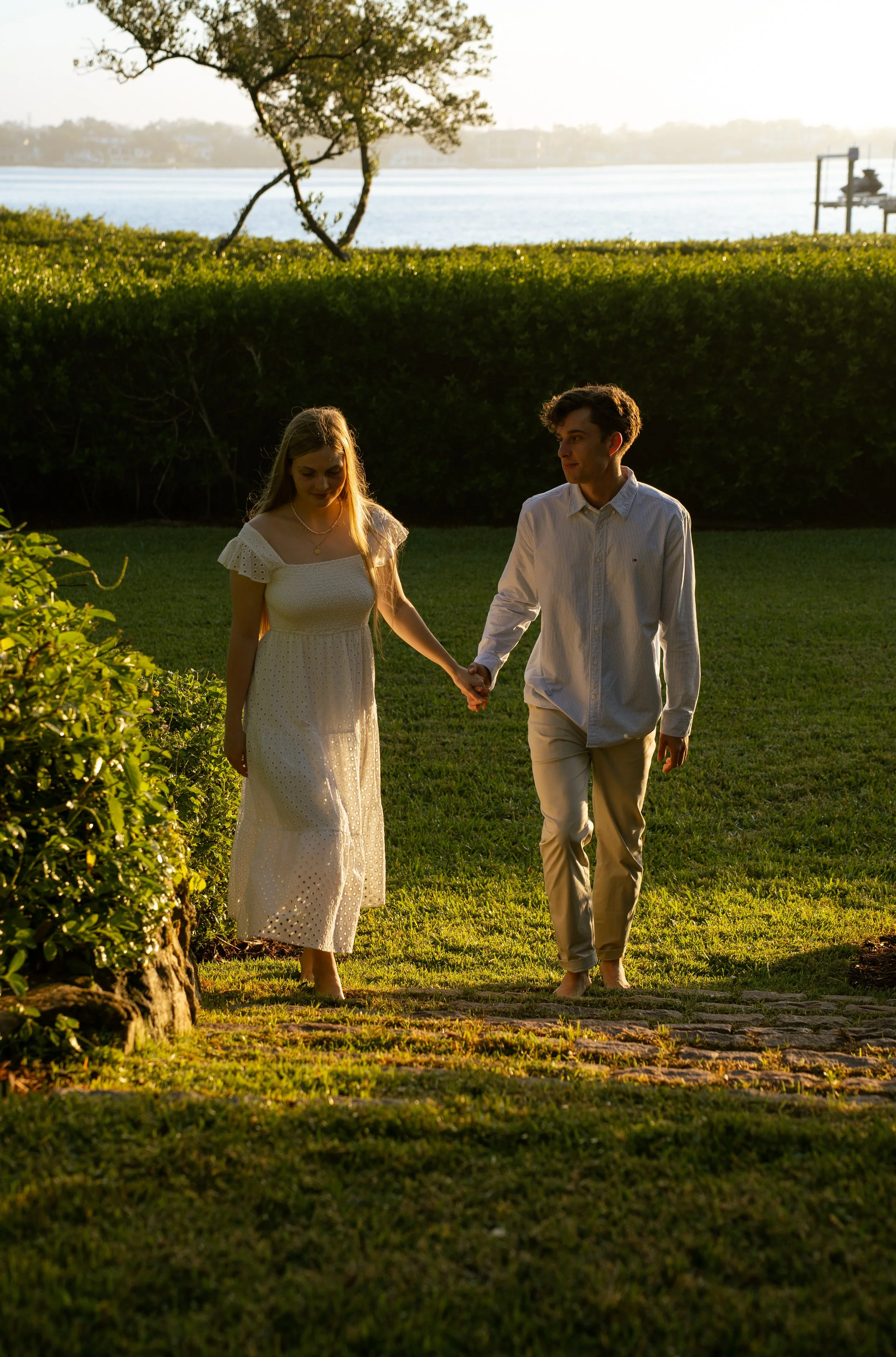 Couple walking hand in hand through a private backyard during a golden hour couples photography session in Sarasota, Florida.
