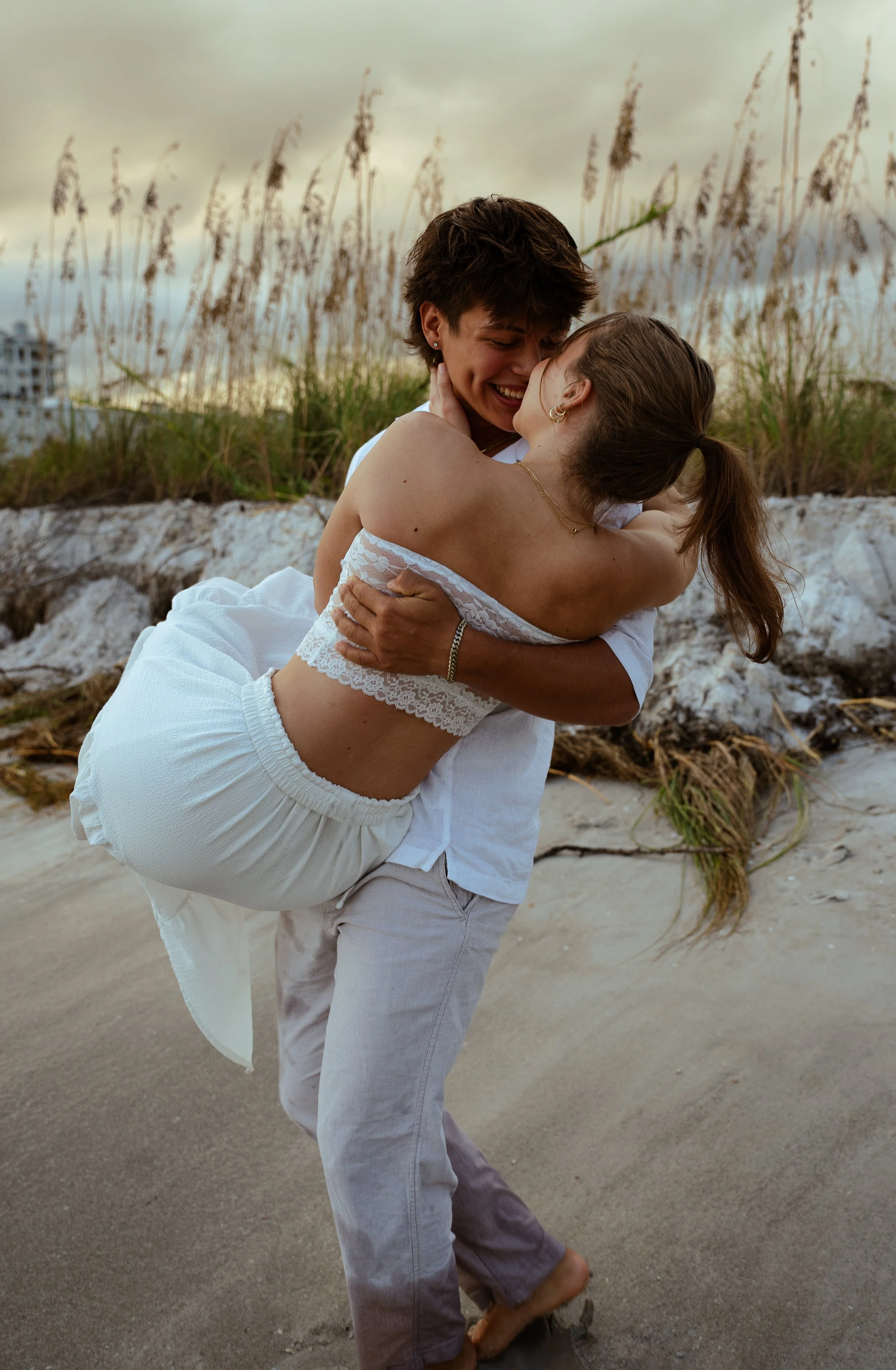 Couple laughing and embracing in the sand during a beach portrait session in Sarasota, Florida.