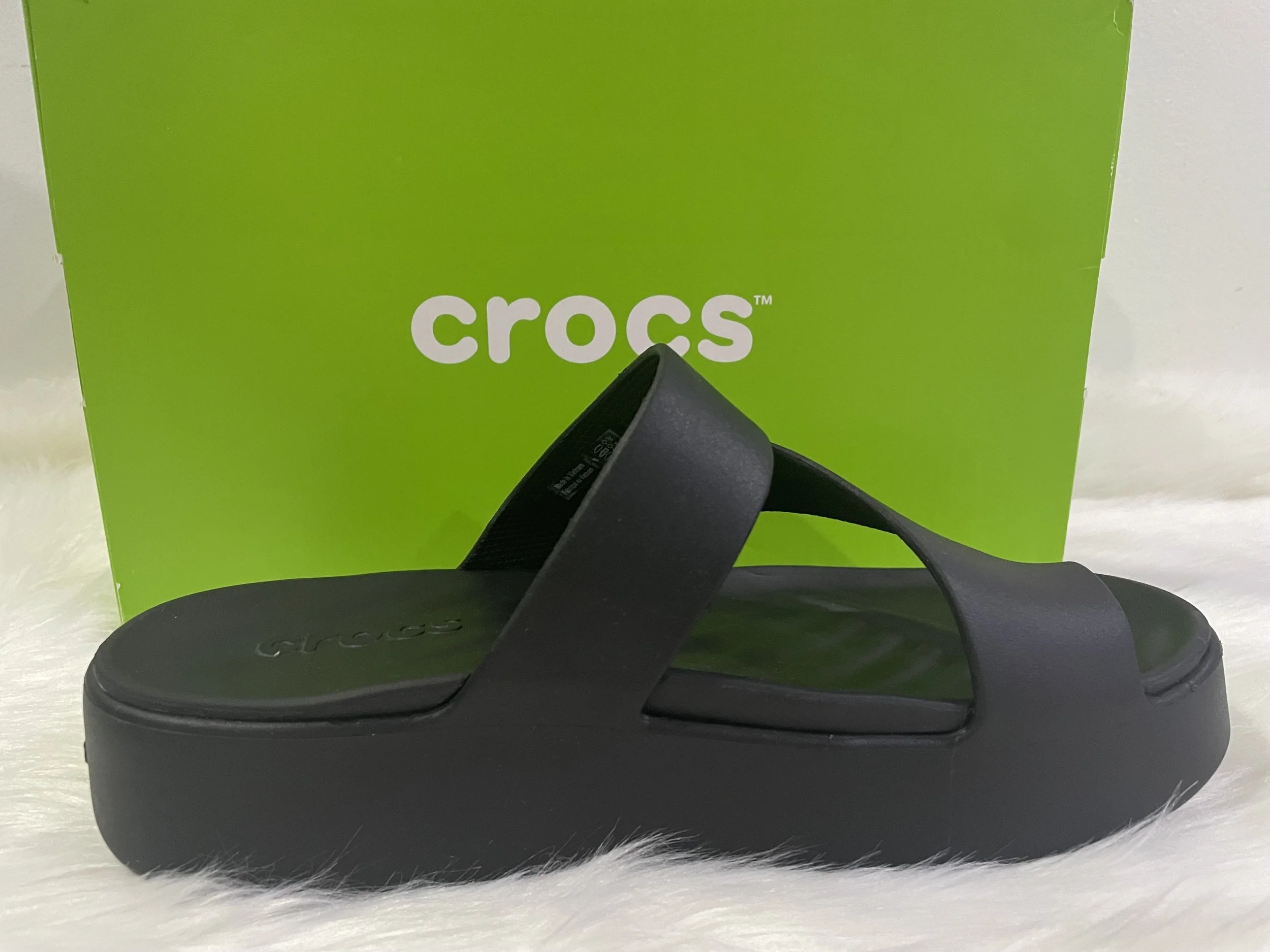 Sandalia Crocs negra sobre fondo de caja verde con logo blanco