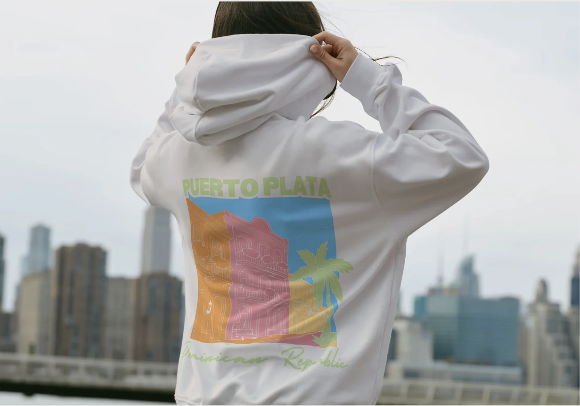 Back of a white hoodie with a colorful graphic of Puerto Plata, Dominican Republic, featuring a building, a palm tree, and the city skyline, with the text 'Puerto Plata' and 'Dominican Republic'.