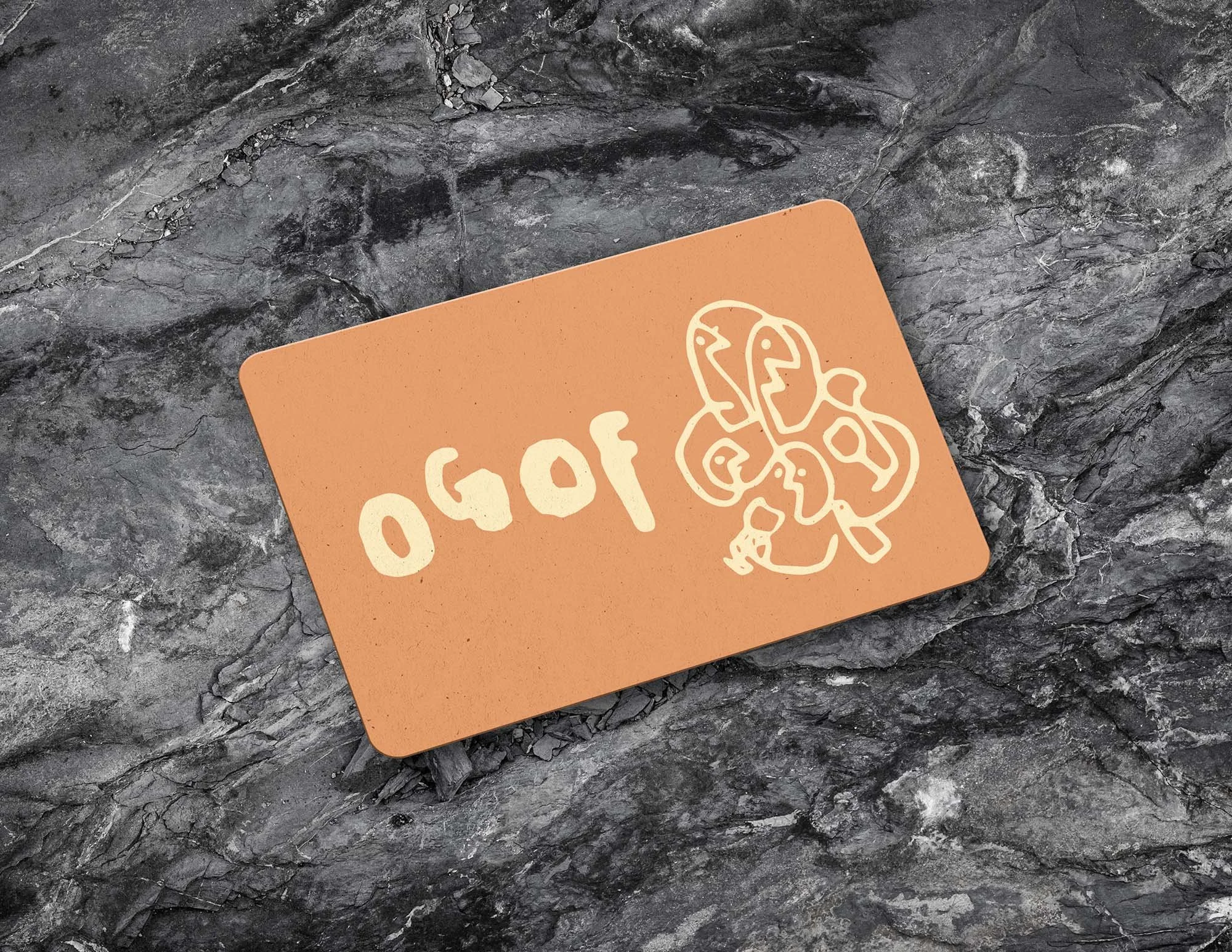 A rectangular orange card with white lines and numbers, and abstract facial doodles, placed on a dark, textured stone surface.