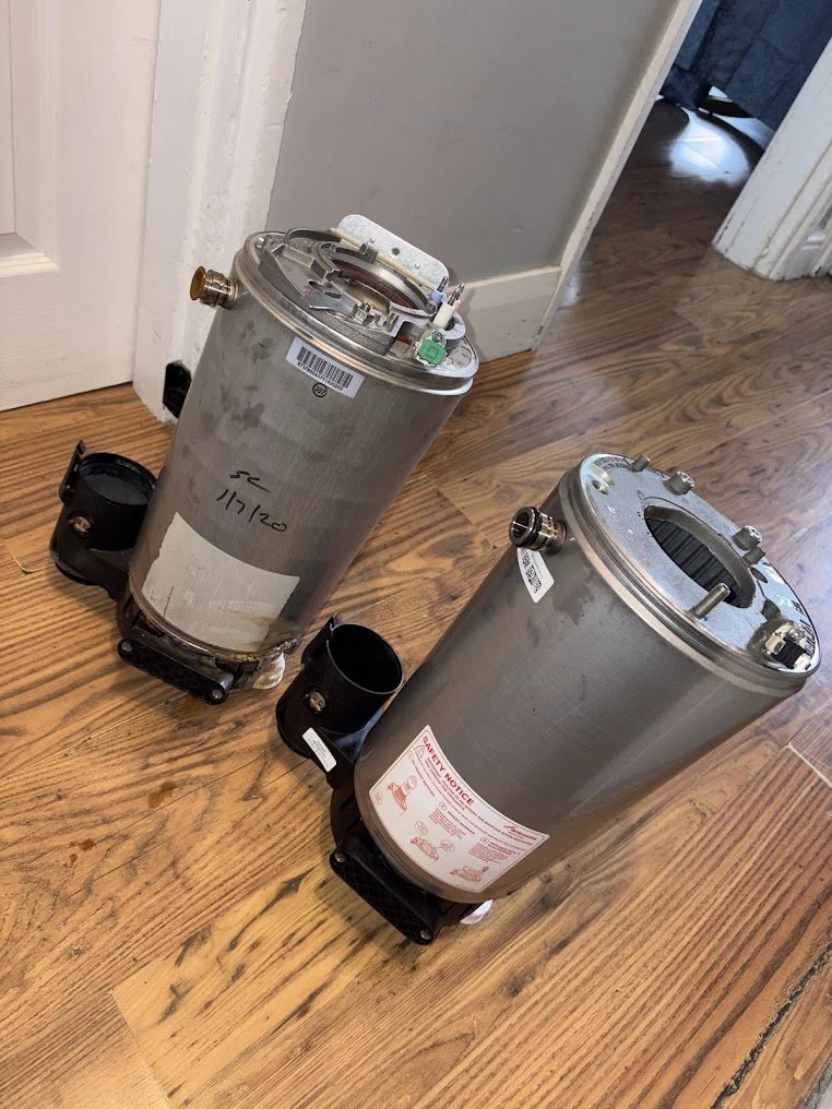 Two pool filter units with labels and markings, placed on a wooden floor indoors.