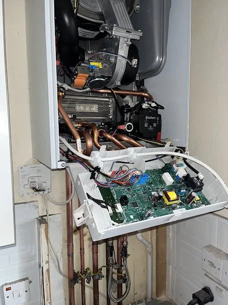 Open boiler with exposed circuit board, copper pipes, and components inside