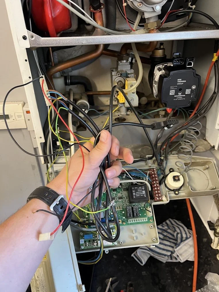 A technician's hand handling multiple wires inside an open HVAC control panel with circuit boards and mechanical components.