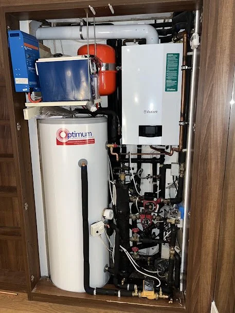 A utility closet containing a water filtration or softening system with pipes, a white tank labeled 'Optimum,' and a white electronic control unit.