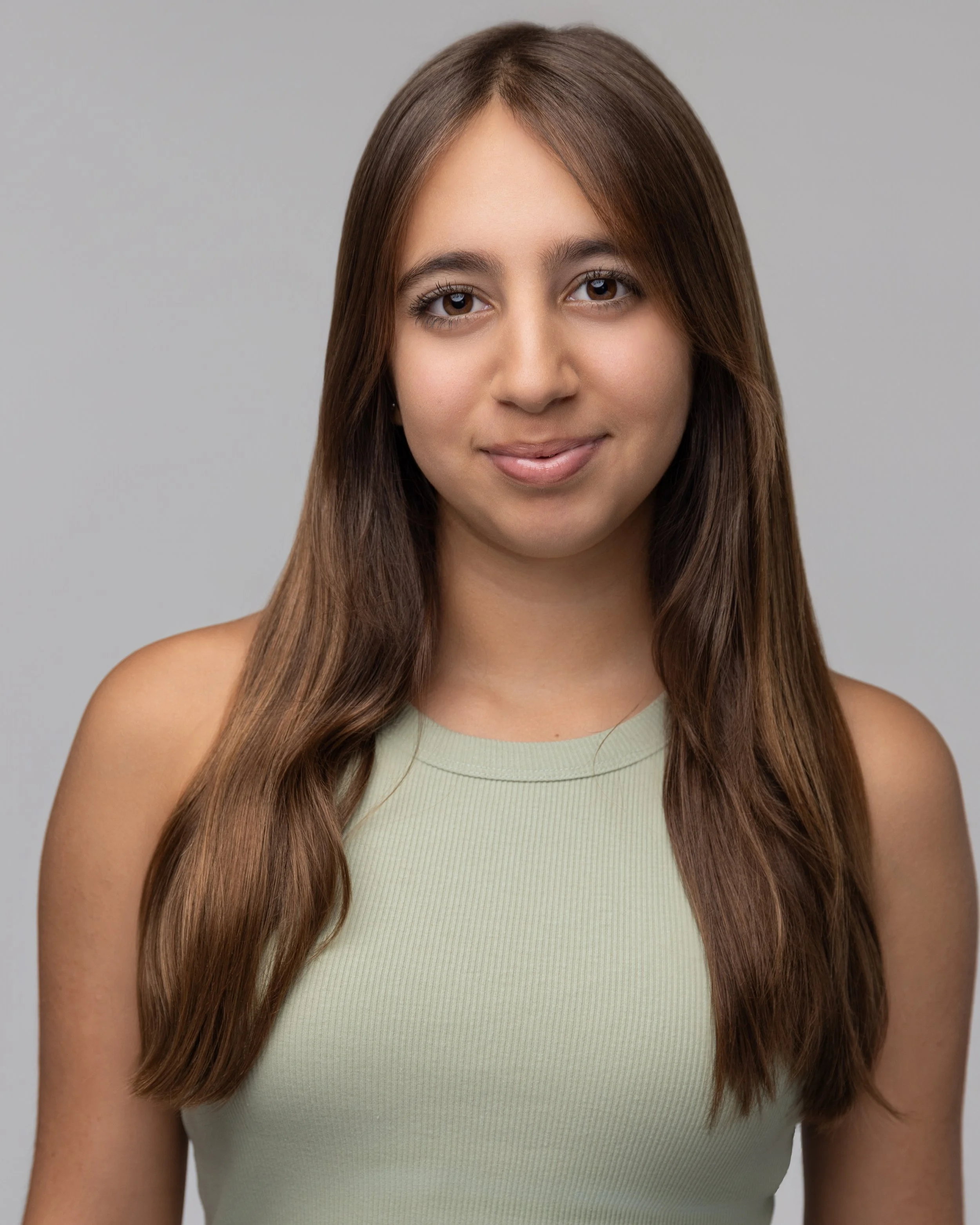 Layla Kazerouni, a young woman with long brown hair wearing a light green sleeveless top, smiling softly, against a plain gray background.