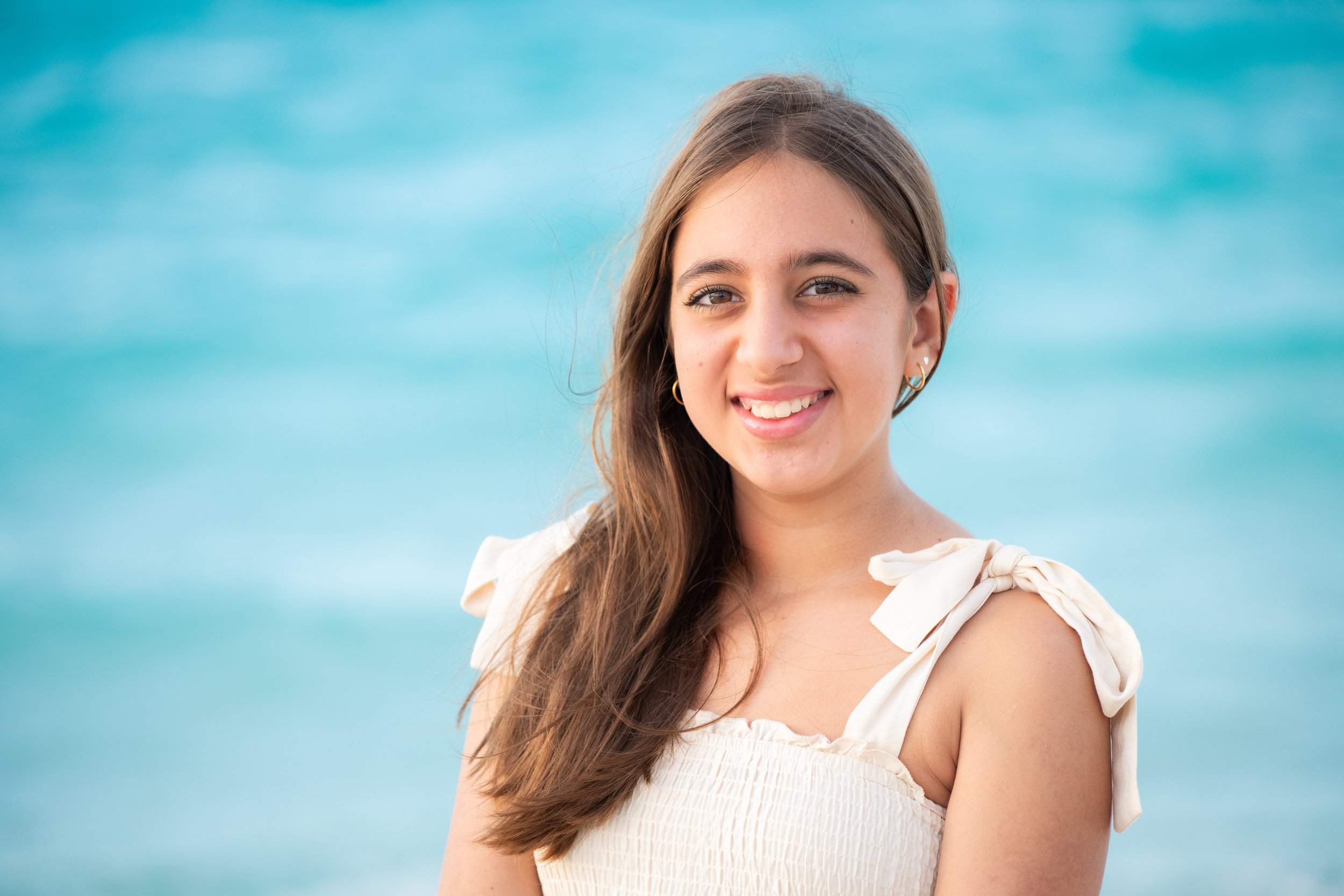 Layla Kazerouni, a young girl with long brown hair smiling at the camera with the ocean in the background.