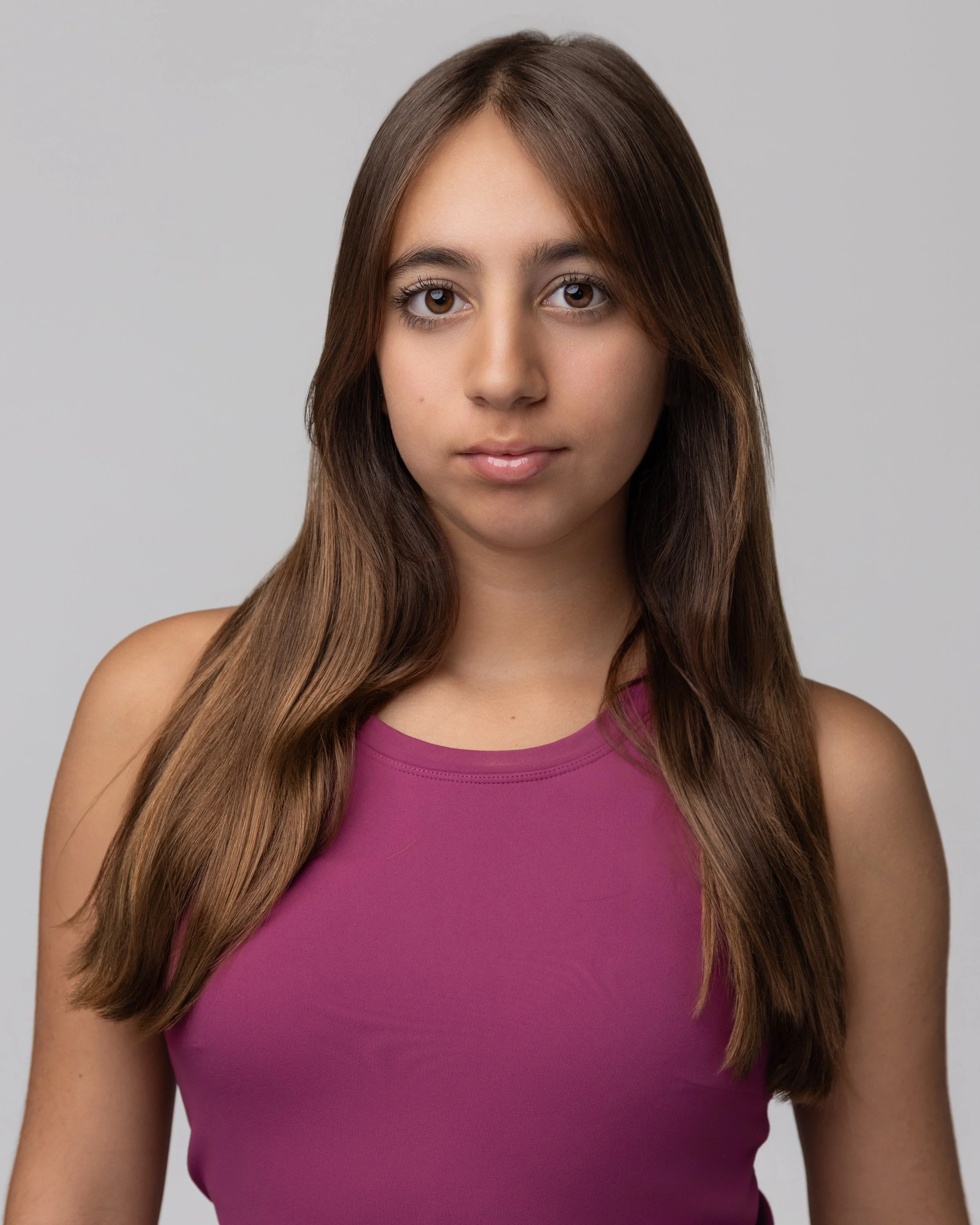 Layla Kazerouni, a young woman with long brown hair and brown eyes, wearing a sleeveless purple top, standing against a plain gray background.
