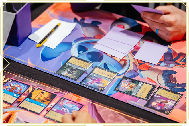 People playing a card game at a table with colorful cards, notes, and a pen, on a vibrant playmat.
