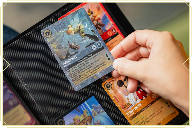 Person holding a Tinker Bell trading card over a black card binder with other colorful cards inside.