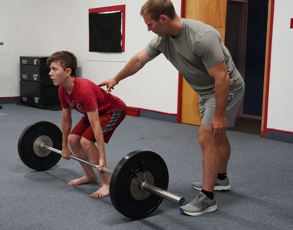 Young athlete deadlifting with hands-on coaching