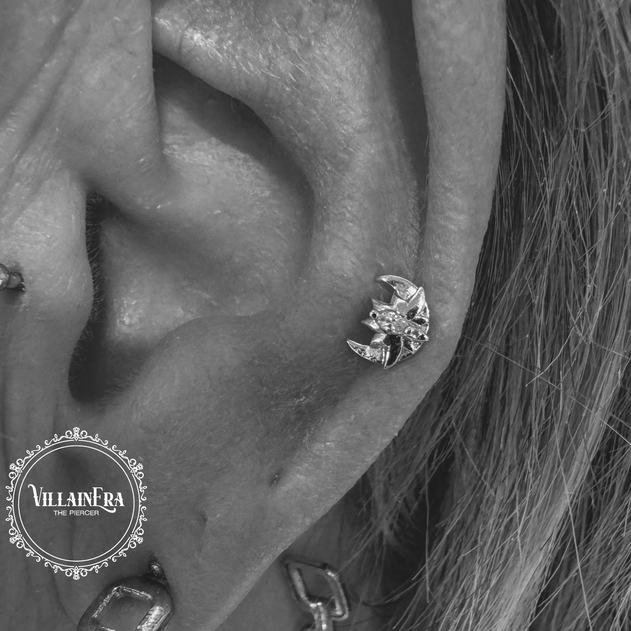 Close-up of a person's ear showing multiple earrings, including a claw-shaped ring earring, with textured skin and hair visible.