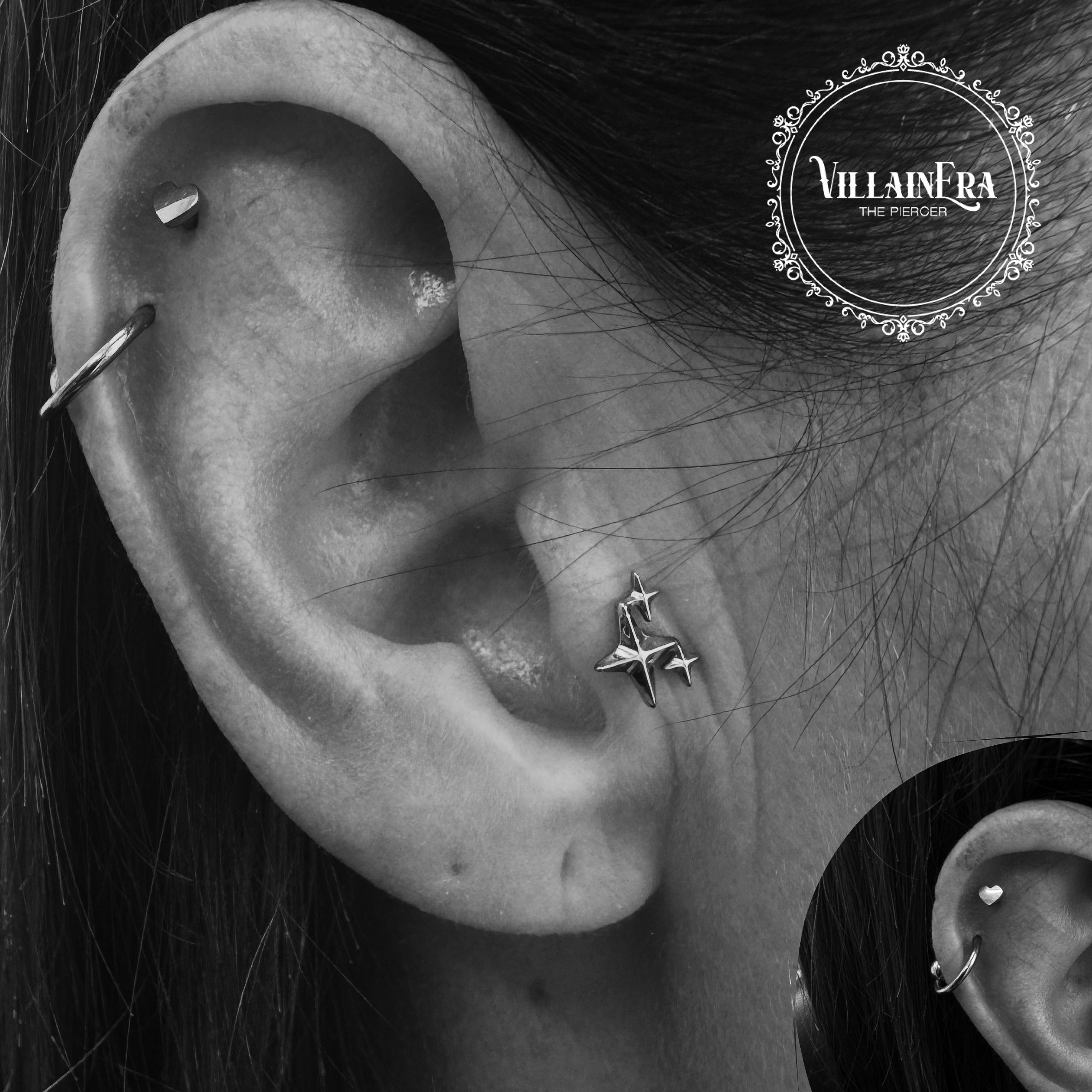 Close-up of a person's ear adorned with multiple earrings, including a star-shaped earring and a small hoop. The image is in black and white, and there is a decorative logo in the top right corner that says "VILLA IN FRA THE PIERCER."