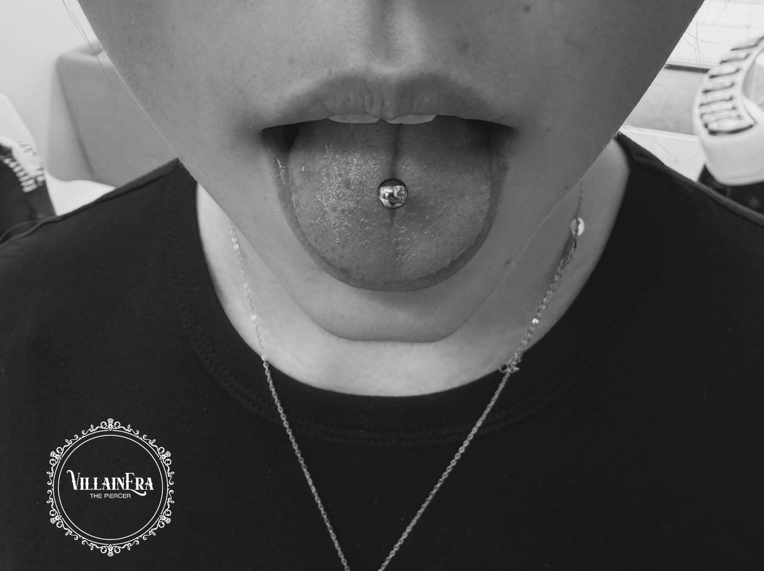 Close-up of a person's mouth with tongue sticking out and a tongue piercing, in black and white.
