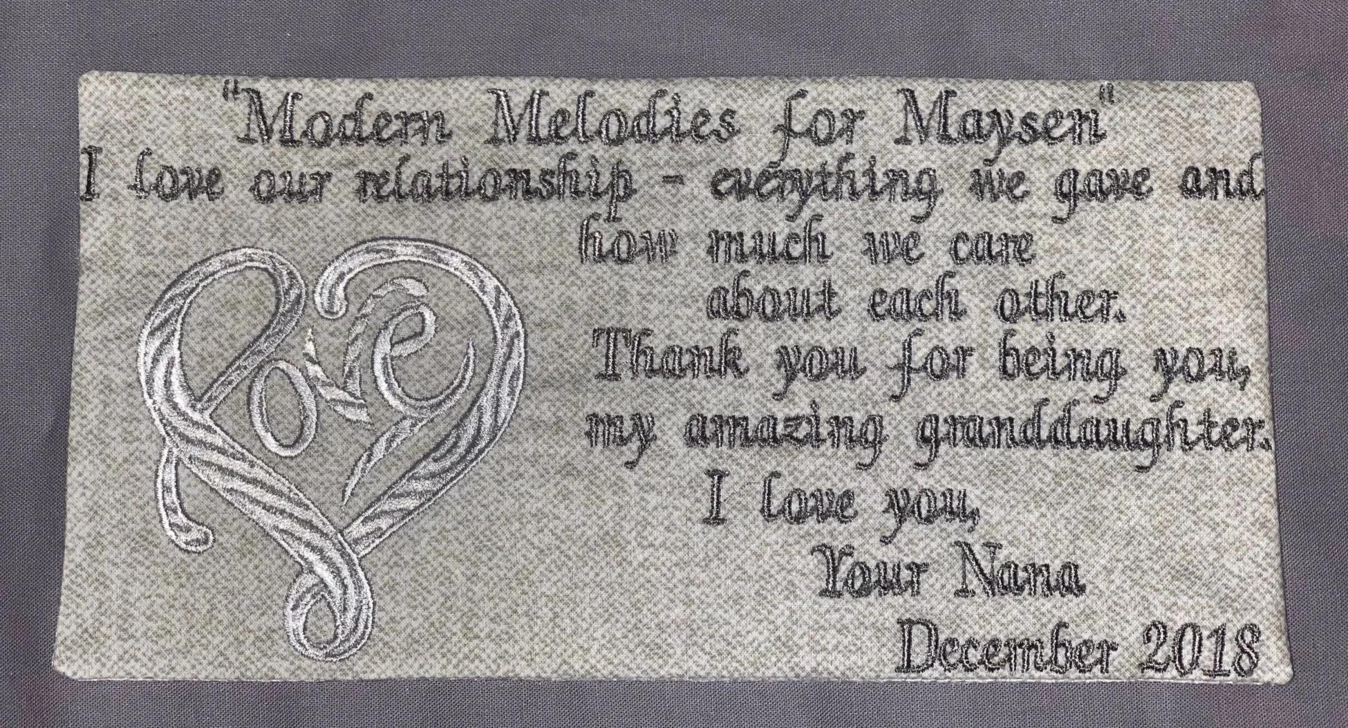 Embroidery of a heart made of intertwined lines with the word 'Love' inside, next to embroidered text expressing love and gratitude for grandmother, dated December 2018.