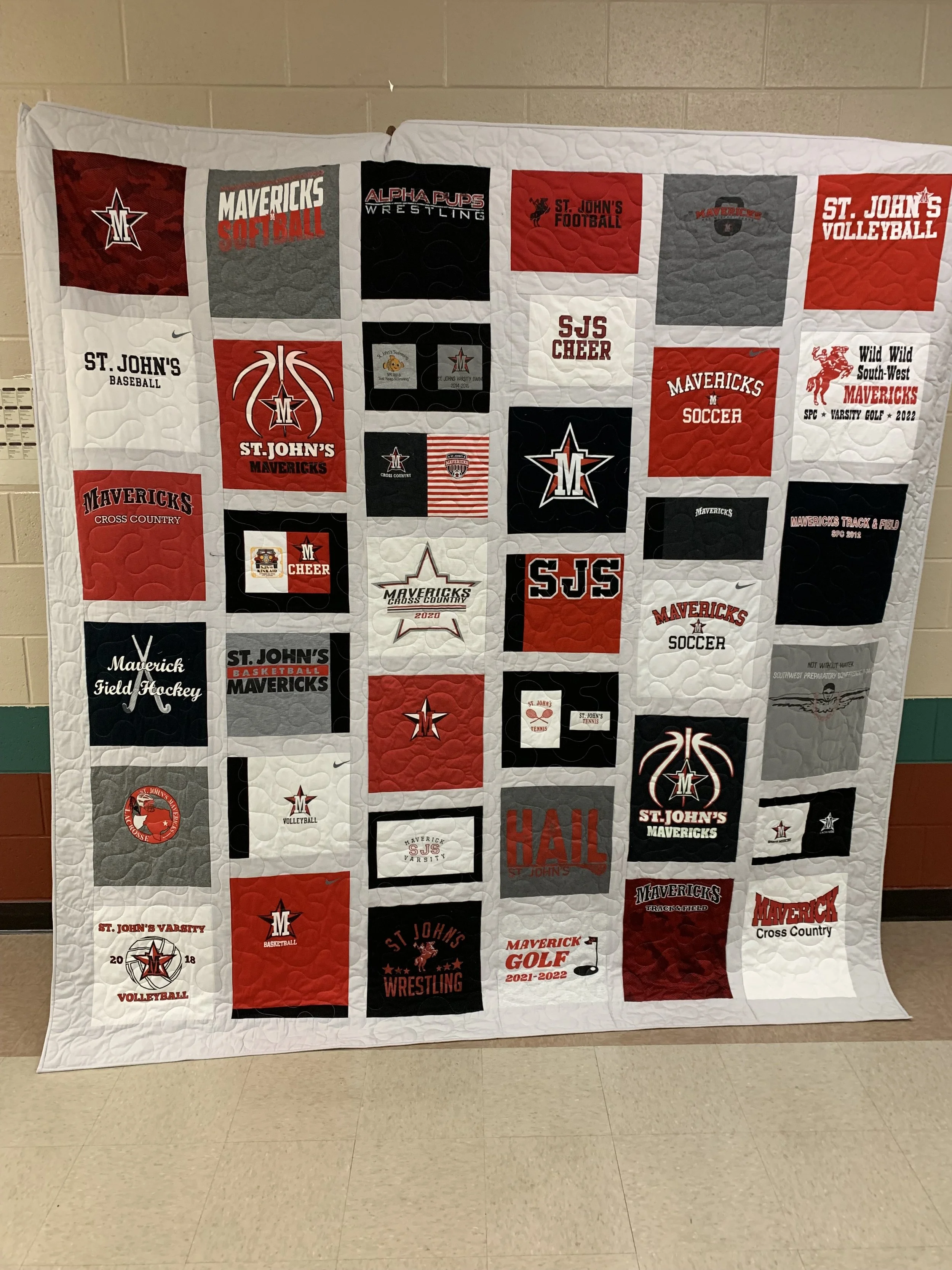 A quilt featuring various school sports team logos and text representing St. John's Mavericks and other teams, with colors red, white, gray, and black.