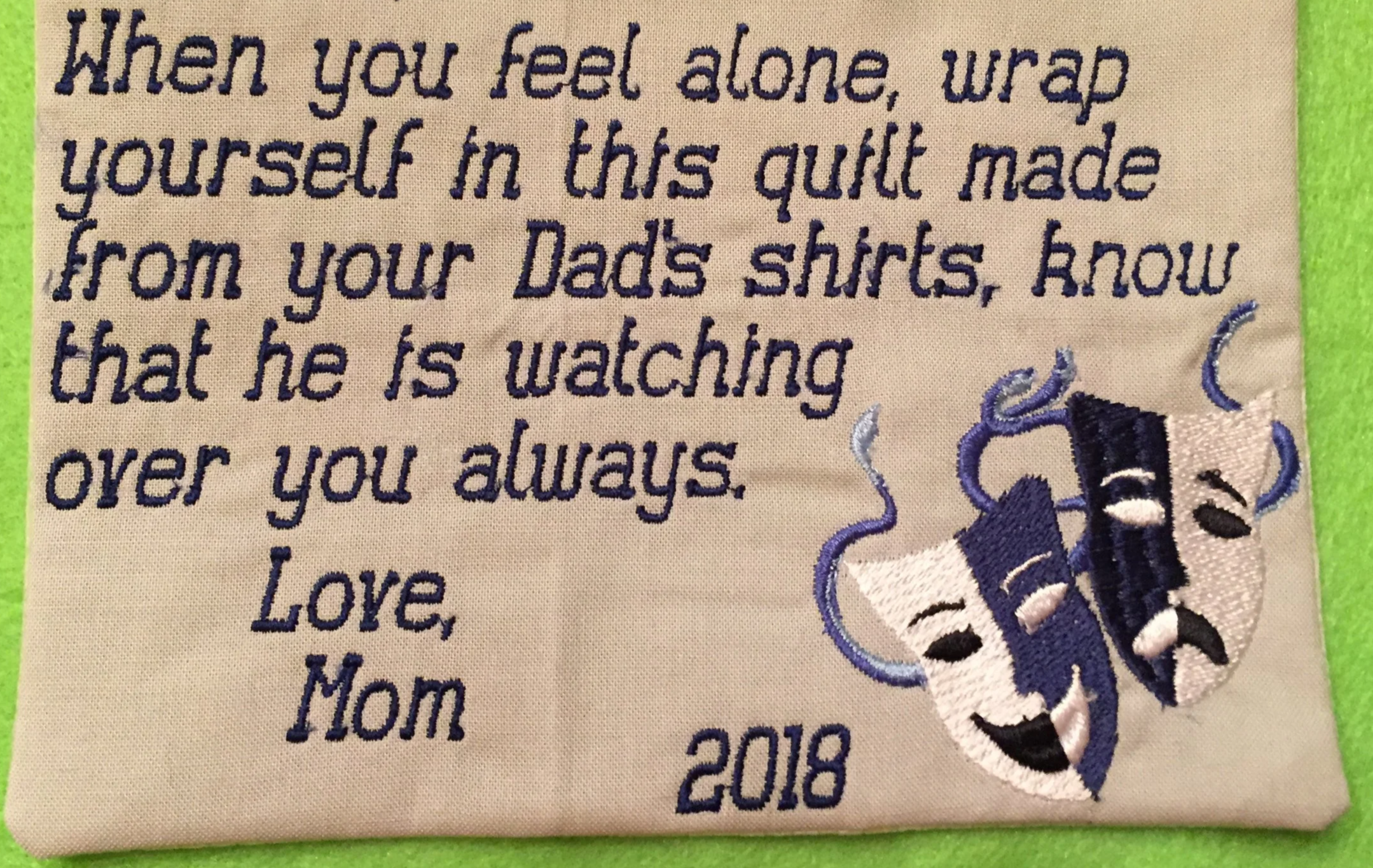 Embroidered fabric with a message about comfort and love, featuring two embroidered comedy and tragedy theater masks, and the year 2018.