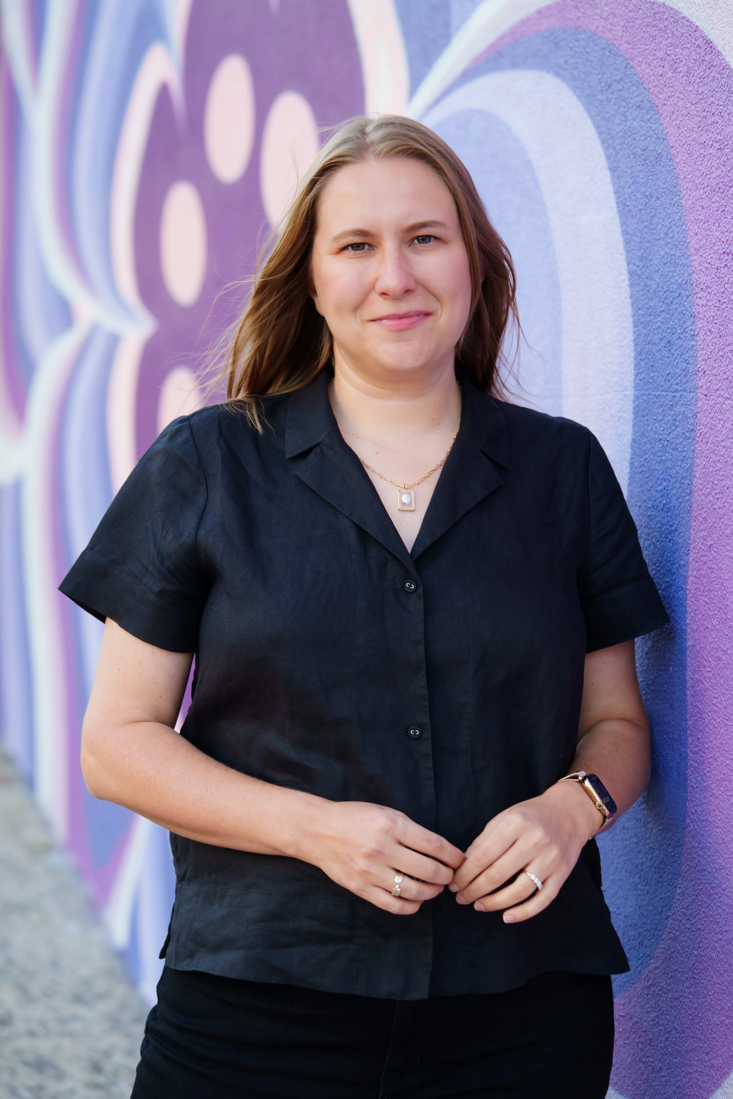 A woman in a black shirt standing in front of a colorful purple and blue mural