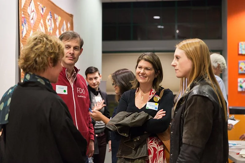 Group of people engaged in conversation at an indoor event, with colorful wall art in the background.