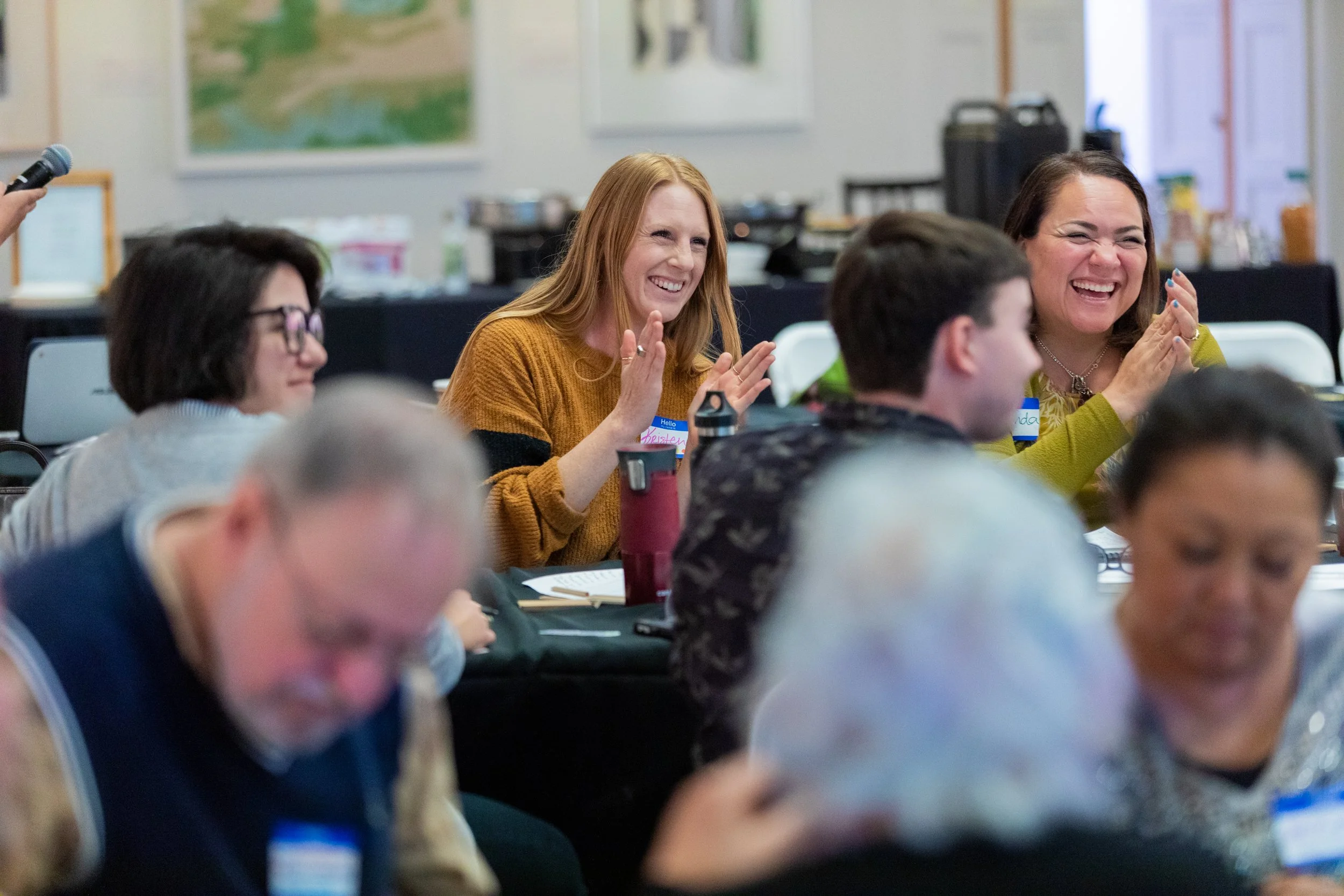 Group of diverse people sitting at a table, smiling, clapping, and engaging during a meeting or workshop.