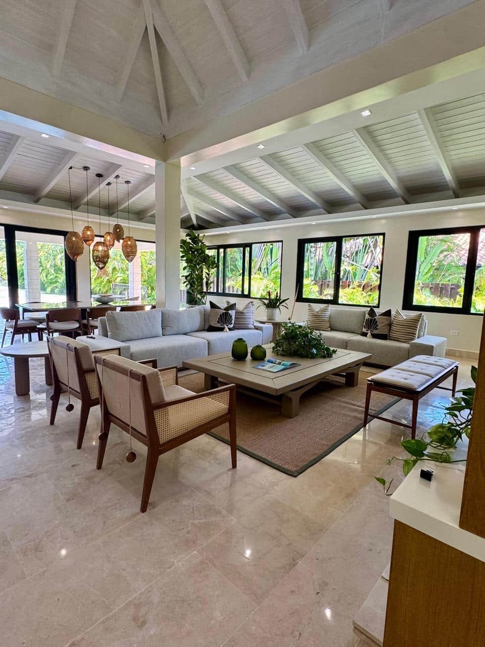 Sofás y sillones en sala luminosa y moderna con muchas plantas verdes y ventanas amplias que dejan ver jardín exterior.