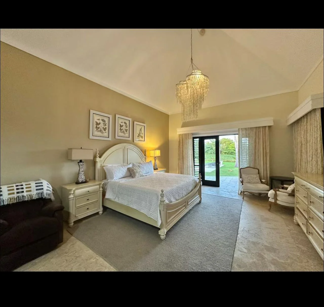 Habitación elegante con cama grande, armarios blancos, sillones, lámparas y vista al jardín.