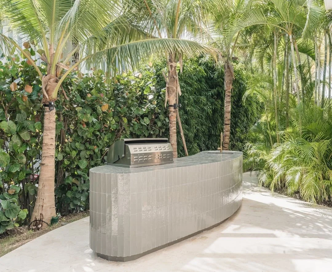 Mostrador de bar con parrilla en un entorno tropical con palmeras y follaje verde.