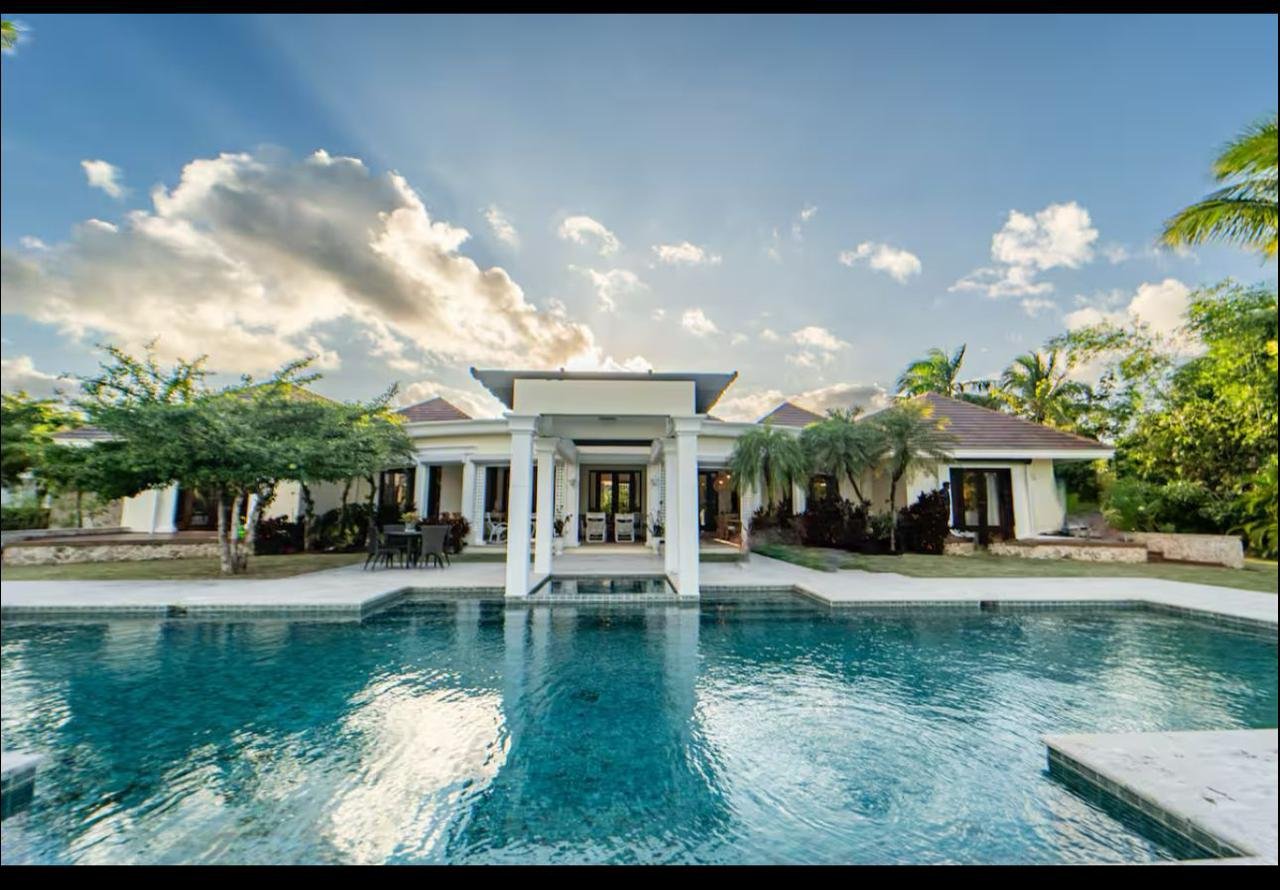 Casa lujosa con piscina y palmeras, jardín y cielo con nubes