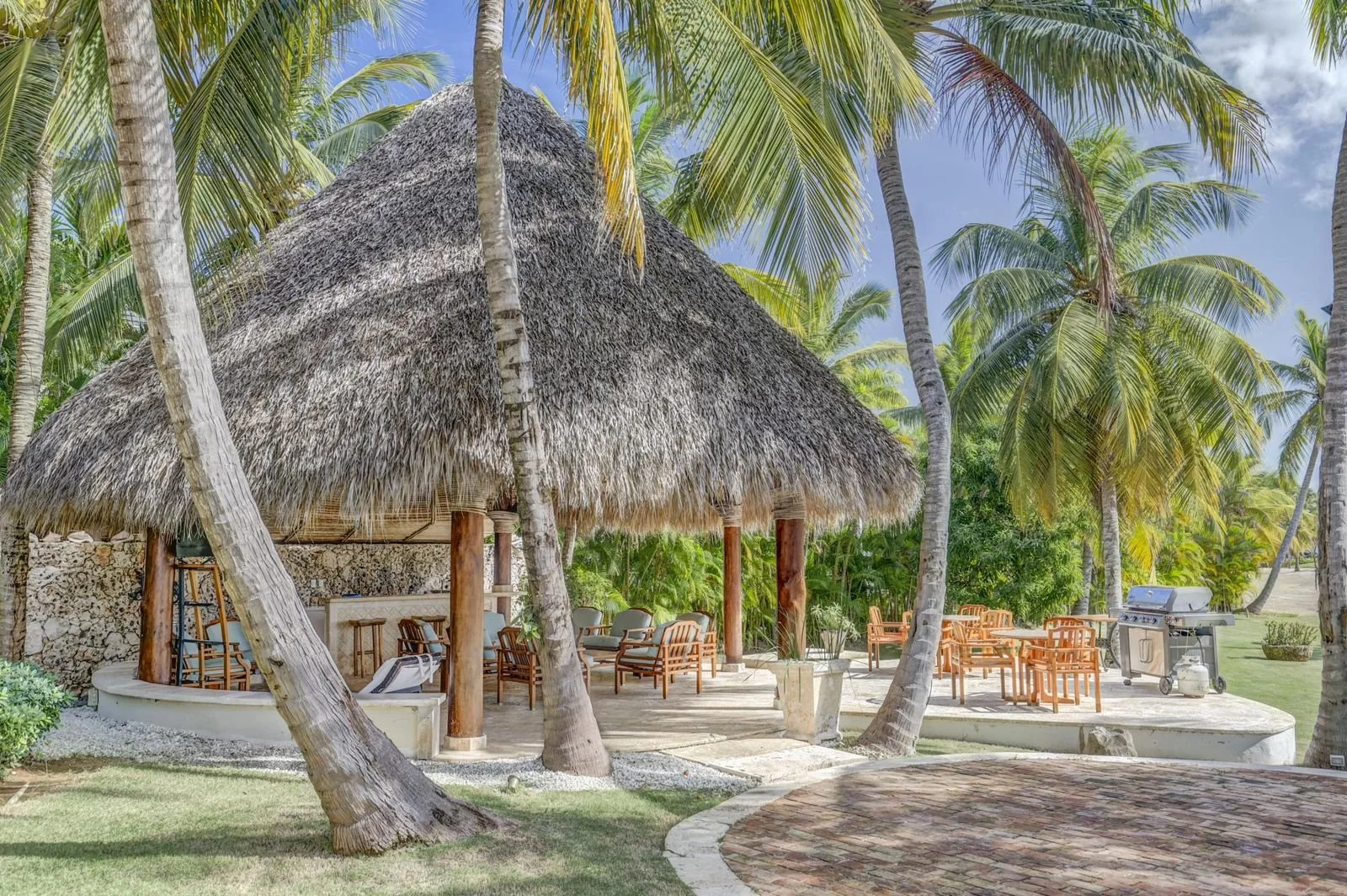 Chiringuito en la playa con sillones, mesas y parrilla, rodeado de palmeras en un día soleado