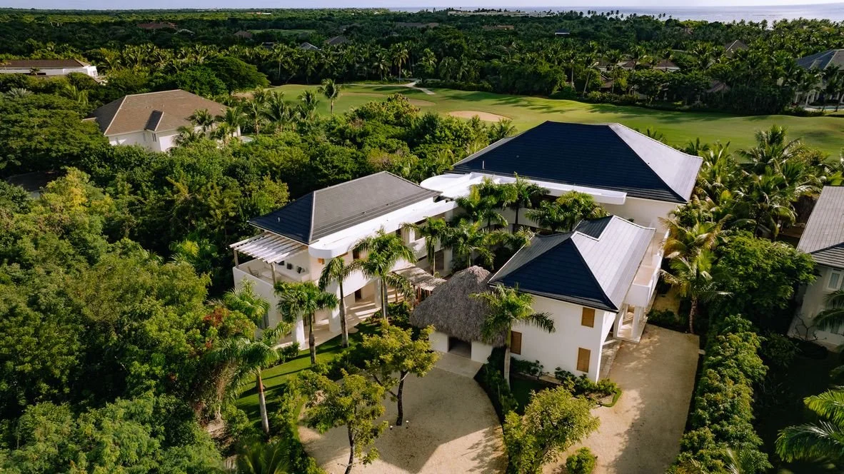 Casa grande rodeada de árboles tropicales y césped, con un campo de golf en el fondo.