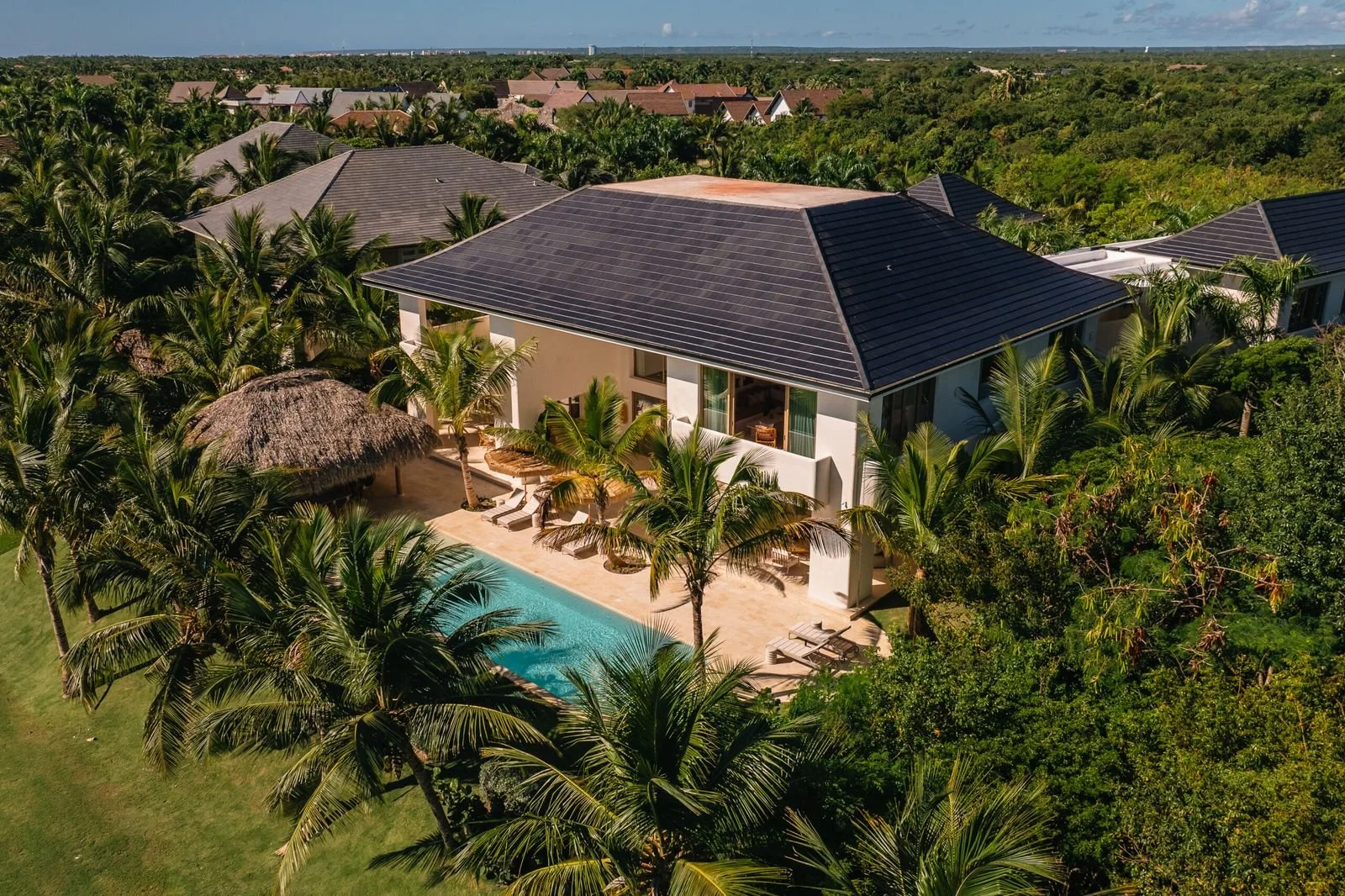 Vista aérea de una casa moderna con piscina en un entorno tropical rodeado de palmeras y vegetación, en un área residencial