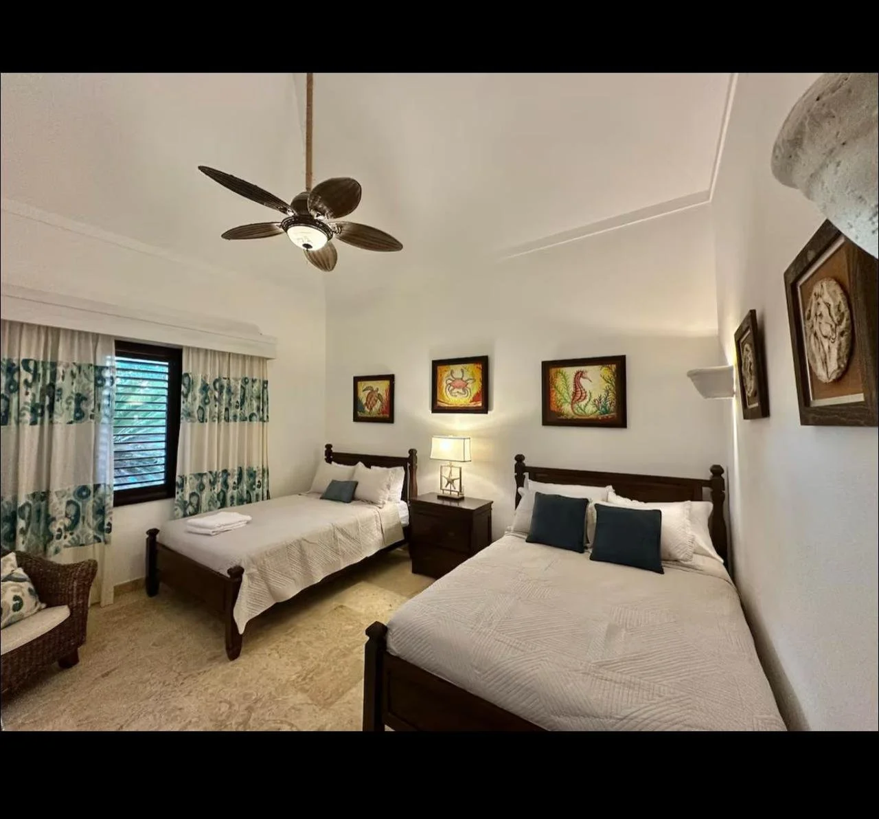 Habitación con dos camas individuales de madera, cuadros coloridos de animales en la pared, cortinas con diseño azul, lámpara y mueble de noche