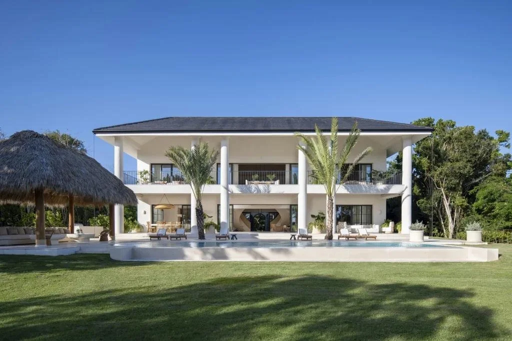 Casa moderna de dos pisos con piscina y palmeras en el jardín, en un día soleado con cielo despejado.