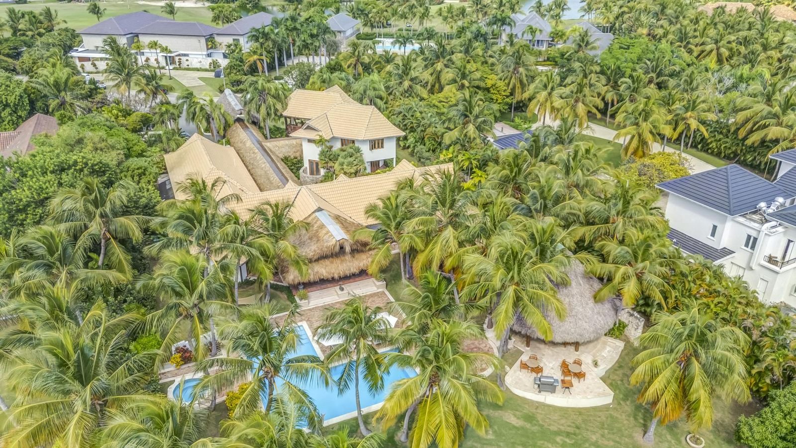 Vista aérea de una propiedad en una zona tropical con muchas palmeras, varias casas, una piscina y áreas de descanso al aire libre.