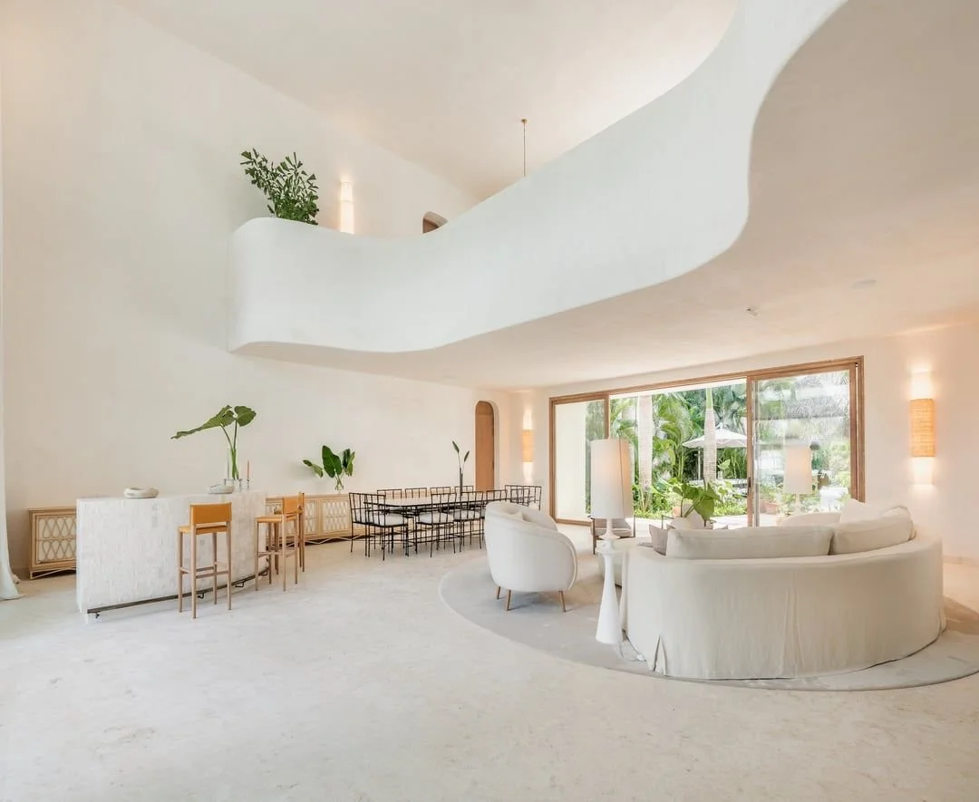 Sala de estar con muebles blancos, ventana grande y vista a un jardín con plantas verdes