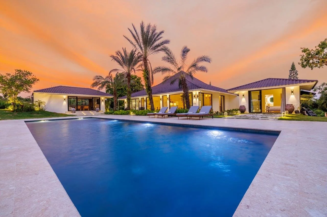 Casa moderna con piscina y palmeras al atardecer.