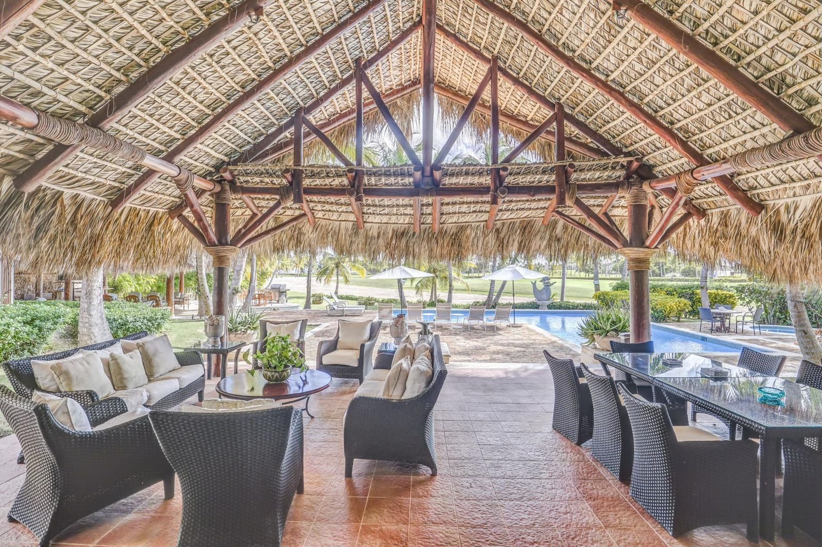 Mirador con techo de caña y muebles de sala y comedor alrededor de la piscina en un área exterior con árboles y palmeras
