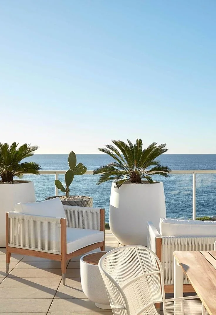 Una terraza con sillas blancas y plantas en macetas grandes con vista al mar