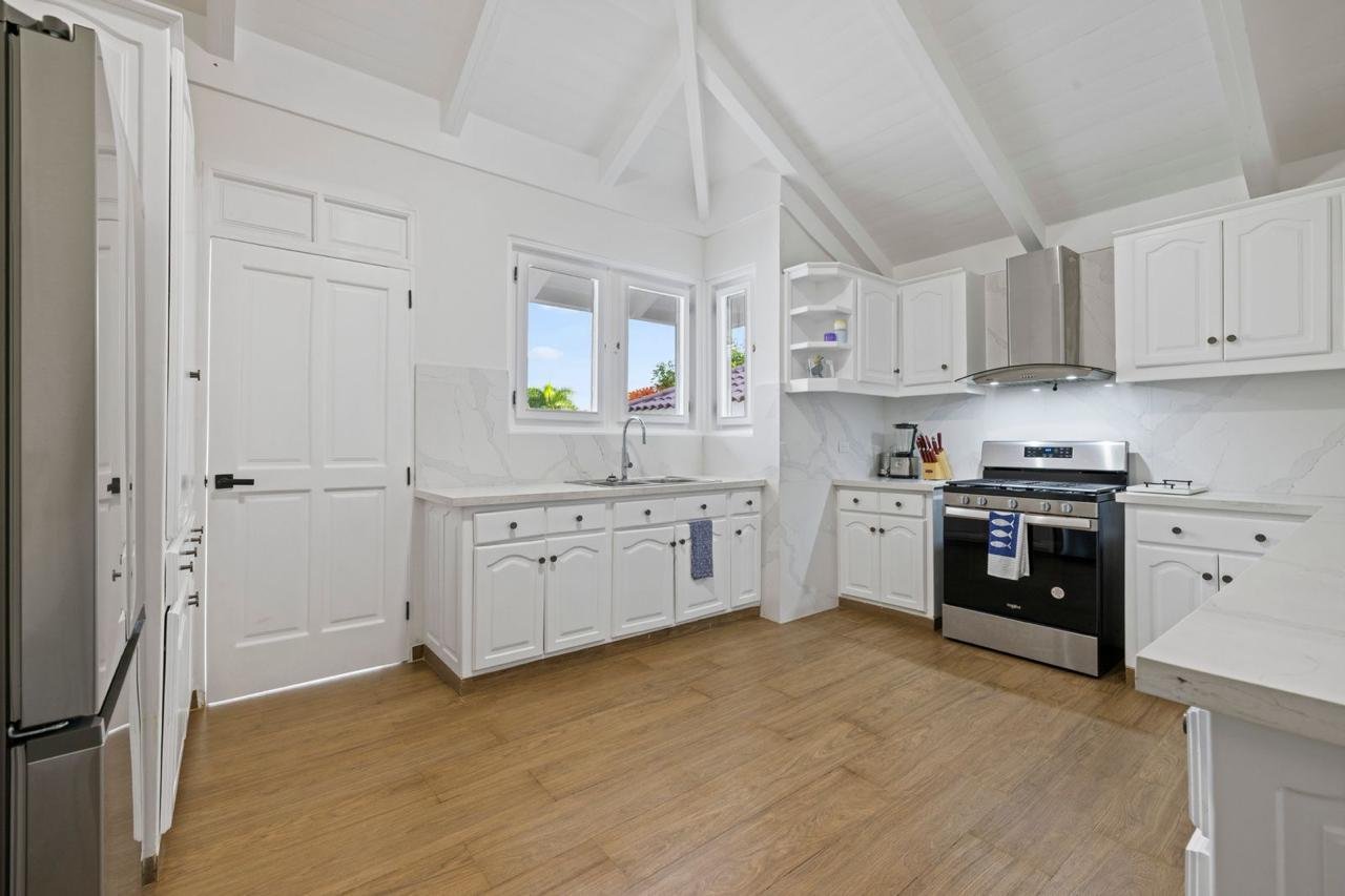 Cocina moderna con gabinetes blancos, estufa de acero inoxidable, ventanas con vista al exterior, y suelo de madera.