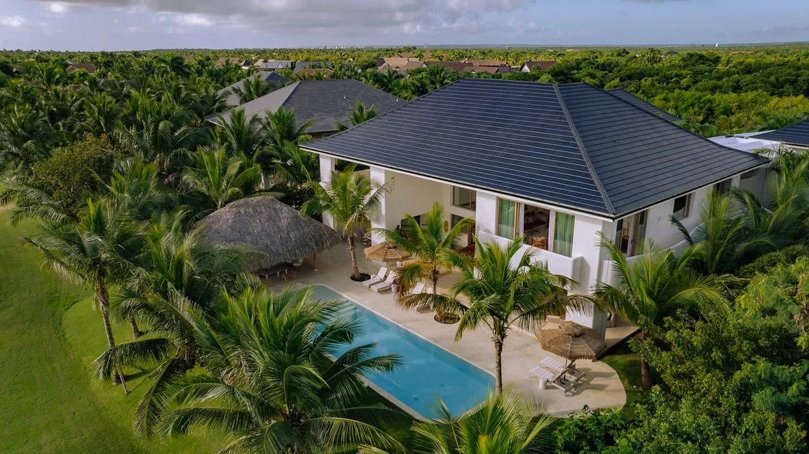 Casa moderna con piscina y palmeras, rodeada de vegetación tropical.