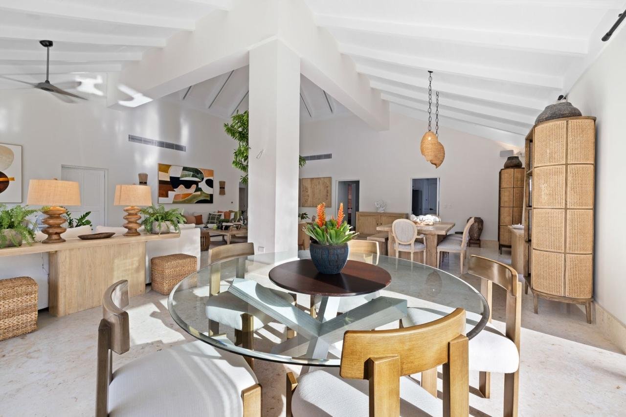 Interior de sala moderna con comedor redondo de cristal, vasos y plantas decorativas.