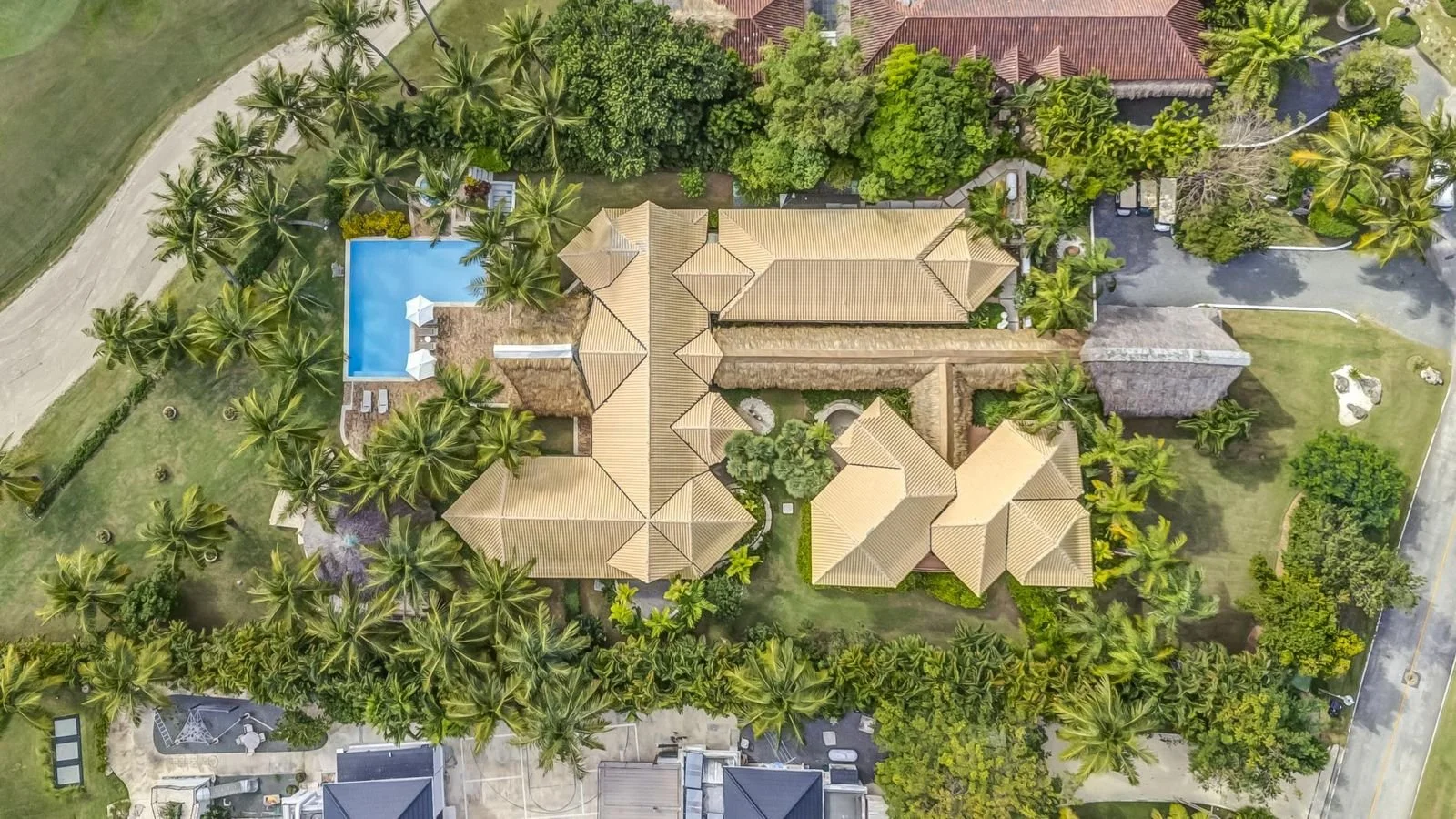 Vista aérea de una propiedad grande rodeada de palmeras y árboles, con piscina, áreas verdes y caminos internos.