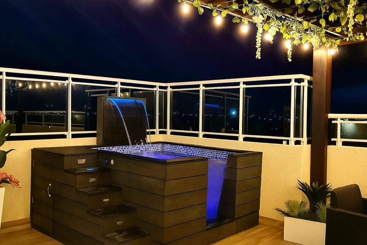 Terraza en la noche con jacuzzi de madera, iluminación decorativa y vista del horizonte.