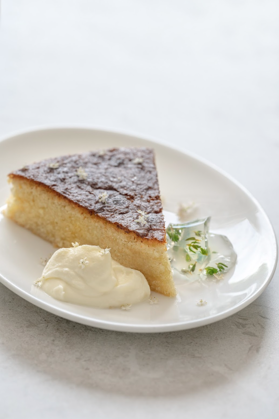 A slice of sponge cake on a white plate with a dollop of cream and edible flowers.