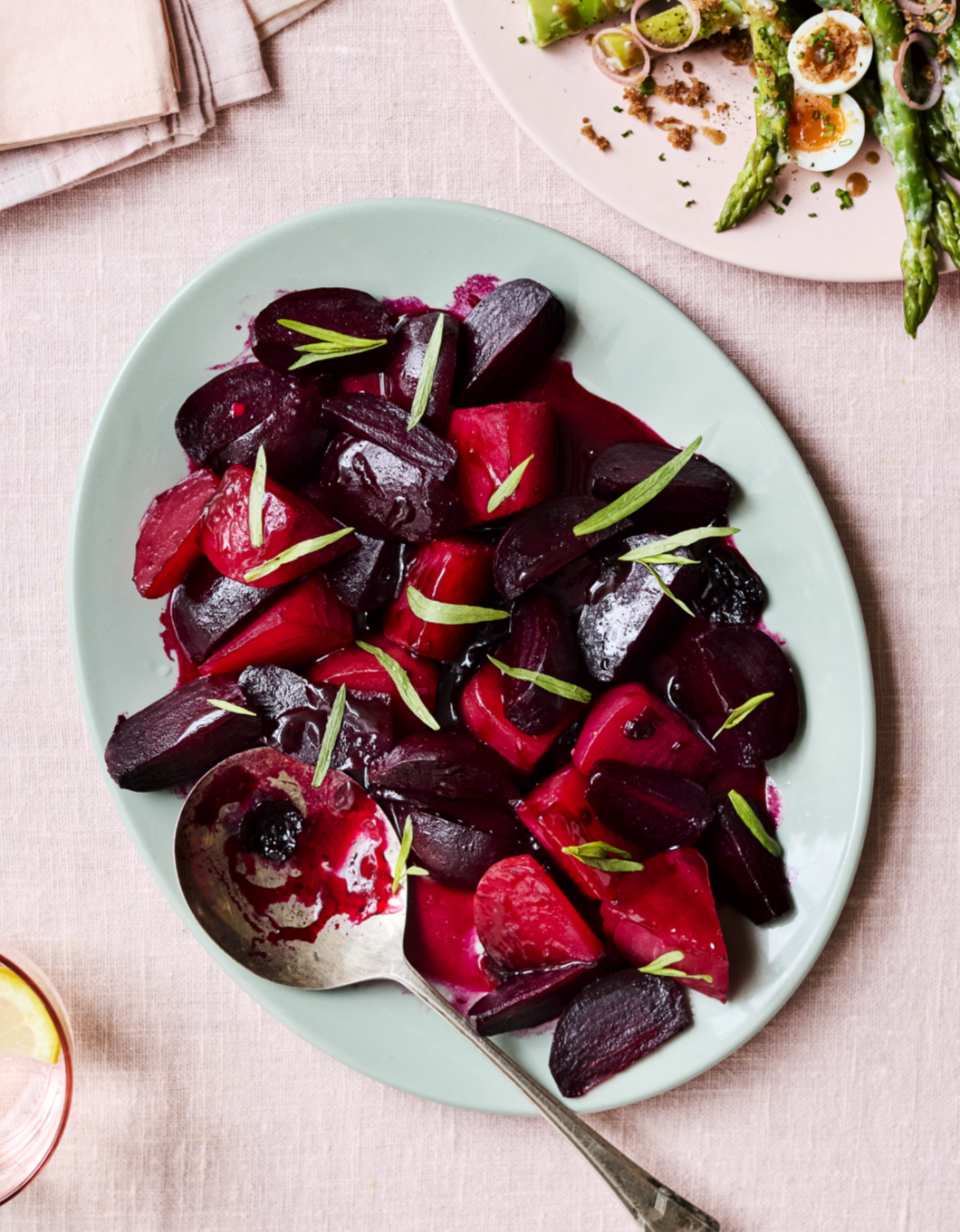 A plate of cooked beets garnished with green herbs, with a spoon resting on the side.