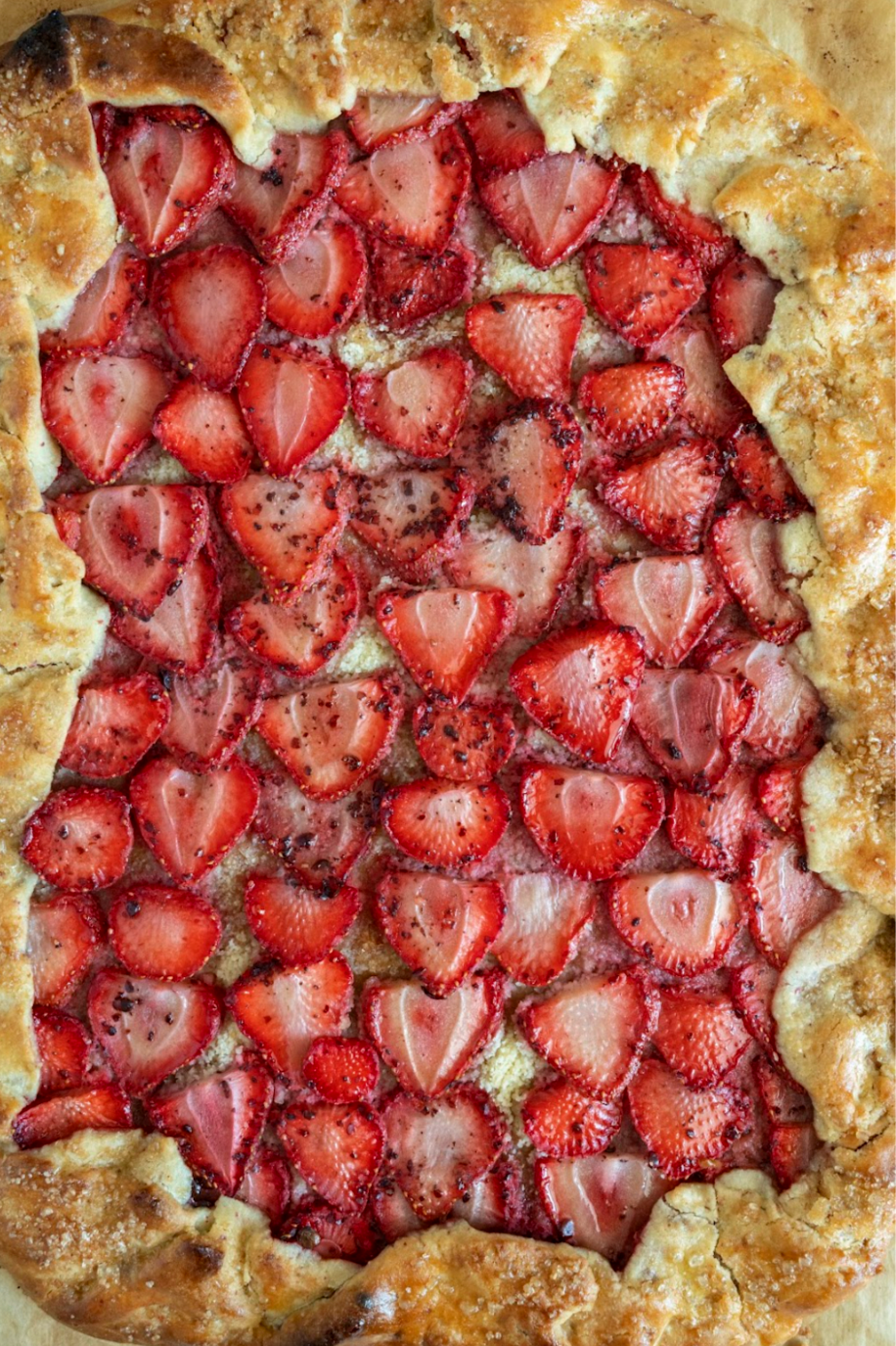 A close-up of a strawberry galette with sliced strawberries on a flaky pastry crust.