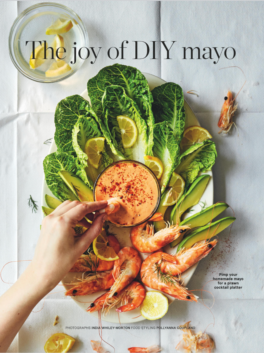 A prawn cocktail platter with shrimp, lemon wedges, romaine lettuce, avocado slices, and a glass of homemade mayo on white tablecloth.