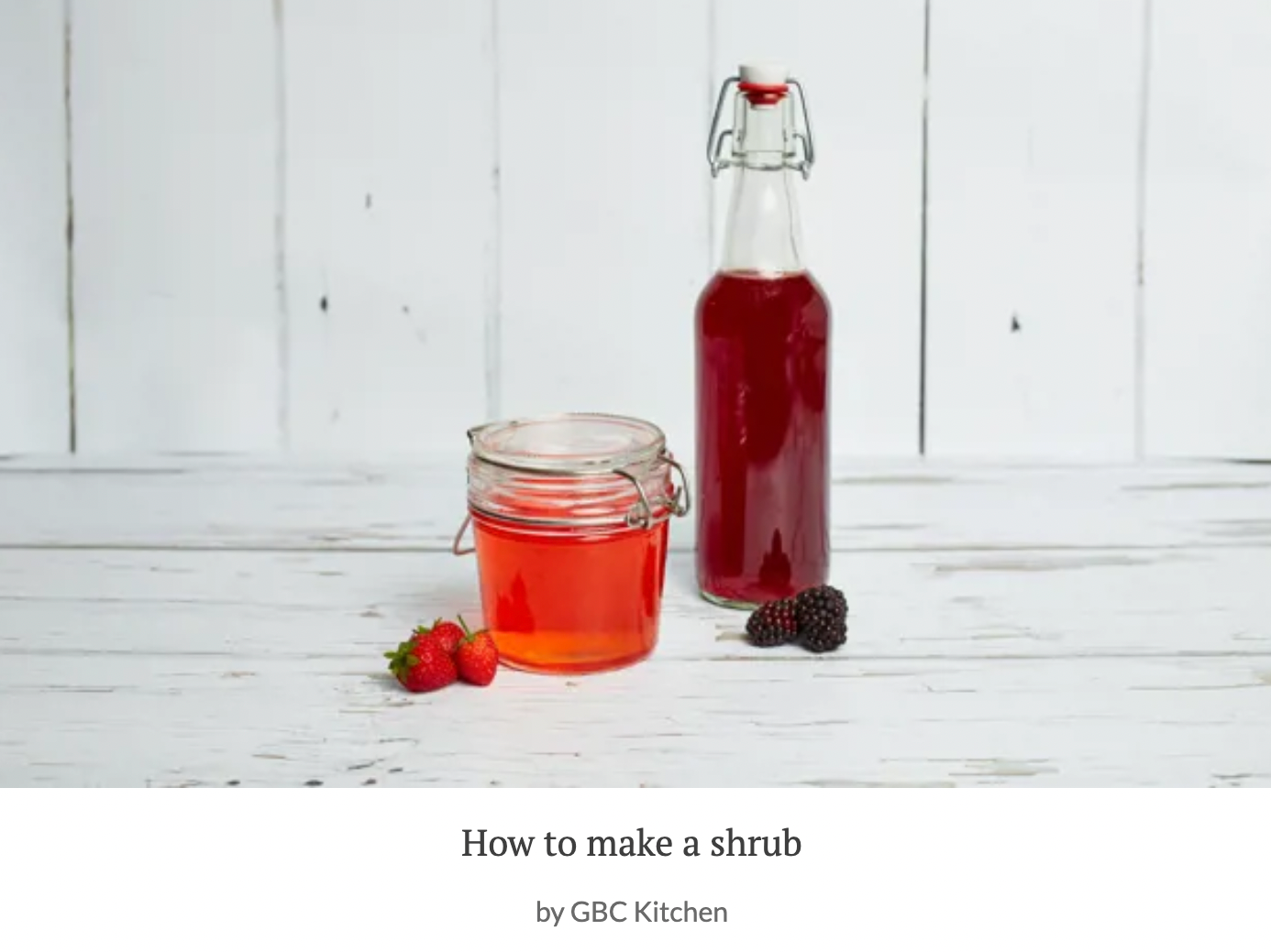 Bottle and jar of homemade berry syrup with strawberries and blackberries on a white wooden surface.