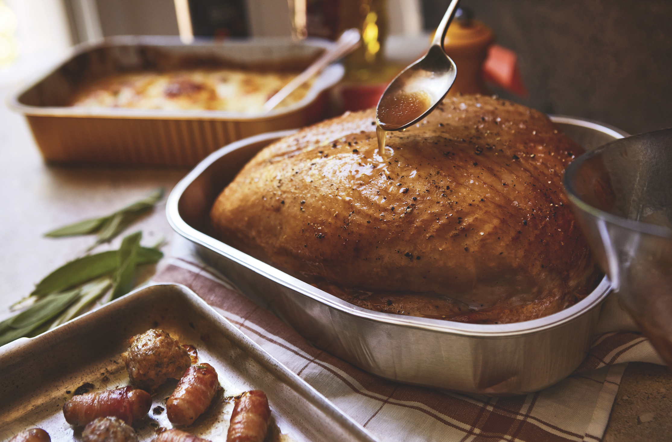 Waitrose turkey crown in foil tray being basted with a spoon. 